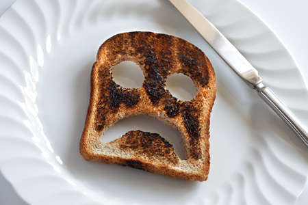 Sad and unhappy smiley made from toasted bread with knife and plateの写真素材