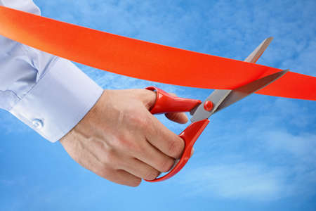 Businessman cutting a red ribbon with a pair of scissorsの写真素材