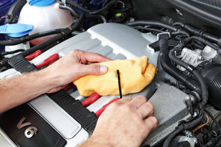 Mechanic holding a dip stick checking the engine oil on a v6 sports carの写真素材