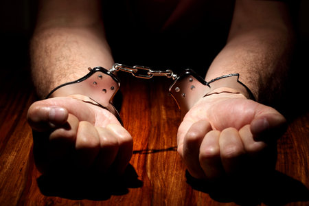 Arrested criminal hands in handcuffs on a wooden desk focus on cuffs
