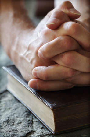 Hands folded in prayer over a Holy Bible resting on a stone baptismal fontの写真素材