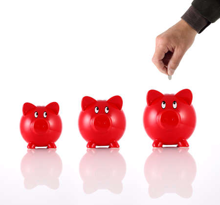 Hand putting coin into three hopeful piggy banksの写真素材