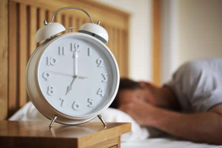 Man sleeping with alarm clock foreground concept for morning, time to wake up or fatigueの写真素材