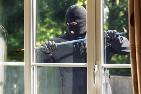 Burglar breaking into a house via a window with a crowbarの写真素材
