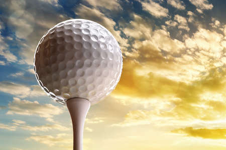 Golf ball on tee about to tee off against a sunset skyの写真素材
