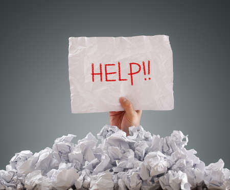 Businessman buried under crumpled pile of papers with a help signの写真素材