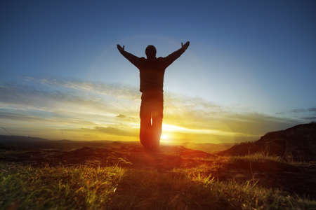 Silhouette of a man with hands raised in the sunset concept for religion, worship, prayer and praiseの写真素材