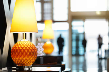 Reception area in luxury hotel close up on lamp with people traveling in and out the front entranceの写真素材