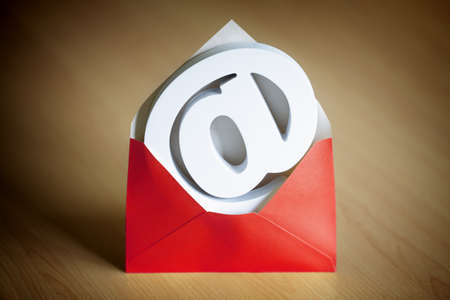 E-mail@ at symbol inside a red envelope on a deskの写真素材