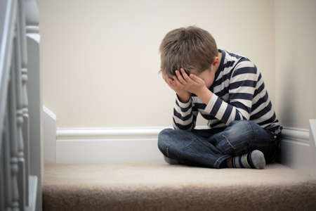 Upset problem child with head in hands sitting on staircase concept for bullying, depression stress or frustrationの写真素材