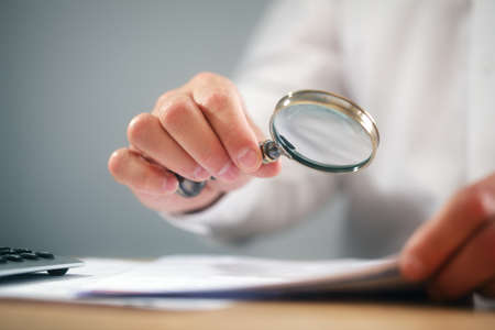 Businessman reading documents with magnifying glass concept for analyzing a finance agreement or legal contractの写真素材