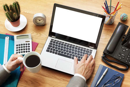 Businessman at a desk in an office typing on a laptop computer with blank white screen ready for contentの写真素材