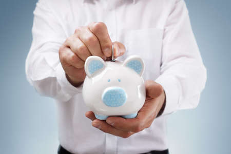 Businessman inserting a coin into a piggy bank concept for business savings, investment or bankingの写真素材