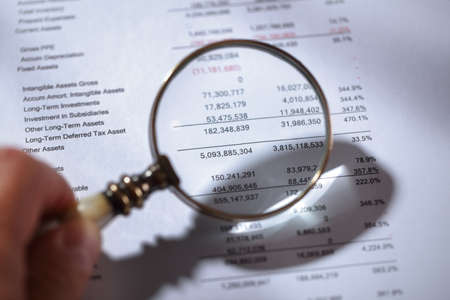 Businessman holding a magnifying glass on a financial report concept for finance, balance sheet, tax or accountingの写真素材
