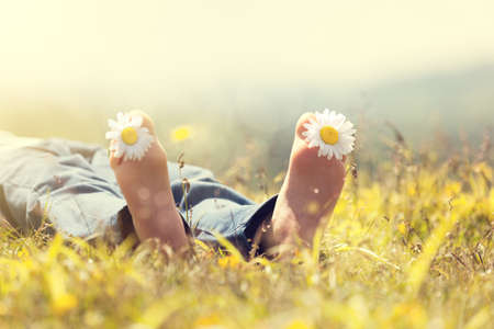 Child with daisy between toes lying in meadow relaxing in summer sunshineの写真素材