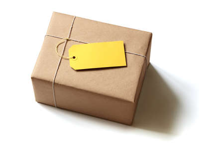 Gift package wrapped in brown recycled paper with blank yellow label isolated on whiteの写真素材