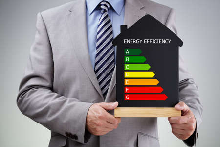 Businessman holding house shape blackboard with chalk energy efficiency rating chart concept for performance, efficiency and environmental conservationの写真素材