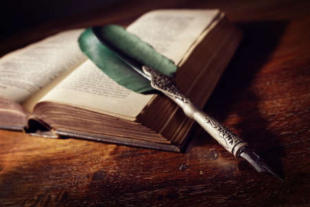 Quill pen resting on an old book on a desk concept for literature, writing, author and historyの写真素材