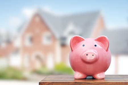 Saving to buy a house, real estate or home savings, piggy bank in front of propertyの写真素材