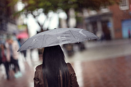 Rain drops falling on a woman holding a black umbrella in a shopping street scene concept for bad...