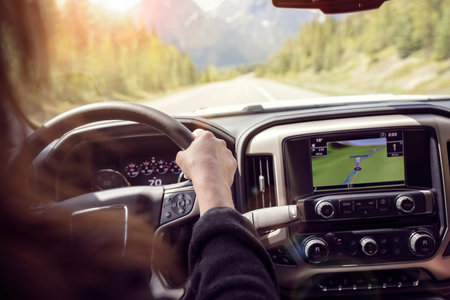 Woman holding the steering wheel driving a car on a rural road through the mountains
