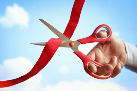 Businessman cutting a red ribbon with a pair of scissors at opening ceremonyの写真素材