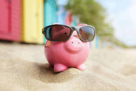Piggy bank on sand beach vacation with sunglasses and bathing boxesの写真素材