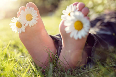 Child with daisy between toes lying in meadow relaxing in summer sunshineの写真素材