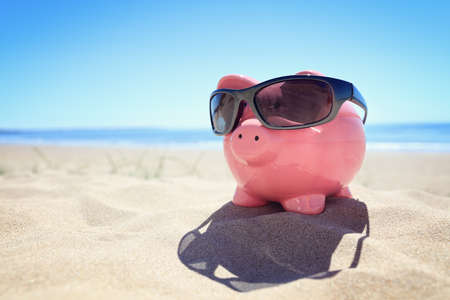 Piggy bank with sunglasses on the beach at the seasideの写真素材