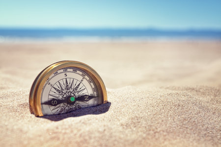 Golden compass buried in the sand on the beach concept for lost or directionの写真素材