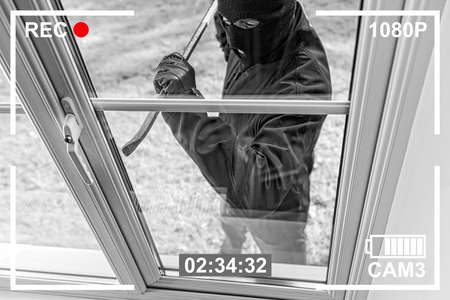 CCTV view of burglar breaking in to home through window with crowbarの写真素材