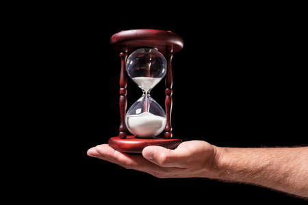 Hand holding hourglass over black background concept for time passingの写真素材