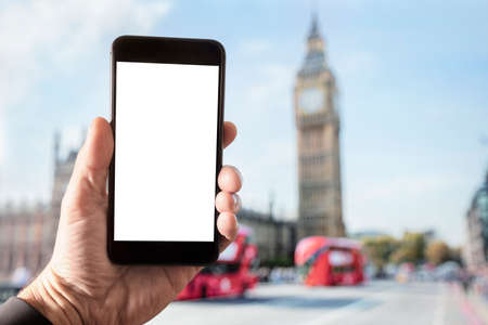 Hand holding smartphone with blank screen in London in front of Big Ben and Houses of Parliament on Westminster Bridgeの写真素材