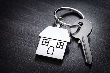 House keys on a house shaped keychain resting on wood background concept for real estate, moving home or renting propertyの写真素材