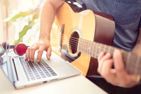 Musician playing acoustic guitar and recording music on computer or learning fom online lessonの写真素材