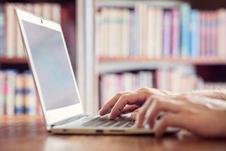 Hands typing on laptop computer in library concept for education, writer or researchの写真素材