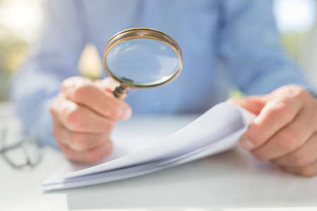 Businessman reading documents with magnifying glass concept for analyzing a finance agreement or legal contractの写真素材