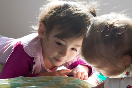 Sisters:4-year-old girl and 1-year-old girl laid in bed watching tablet