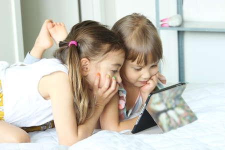 Curious little girl sisters having fun using digital tablet , happy preschool smart kid playing with computer looking at screen watching cartoons online at homeの写真素材
