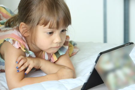 Curious little girl having fun using digital tablet , happy smart kid playing with computer looking at screen watching cartoons online at homeの写真素材