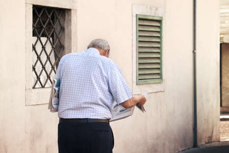 Lonely senior reading newspaper, he's alone and he's walking on the streetの写真素材