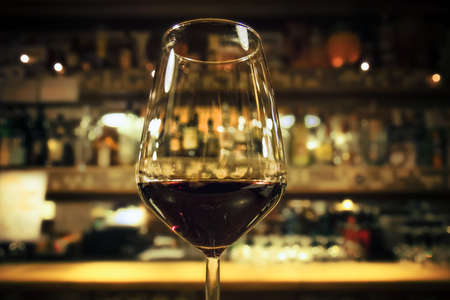 glass of red wine, drink with blurred bottles of alcohol on background (warm tone)の写真素材