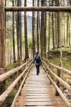 young woman crosses a bridge, she is walking in a forest with backpack
