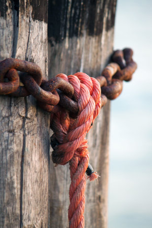 vertical image of nautical rope, red knot on rusty chain