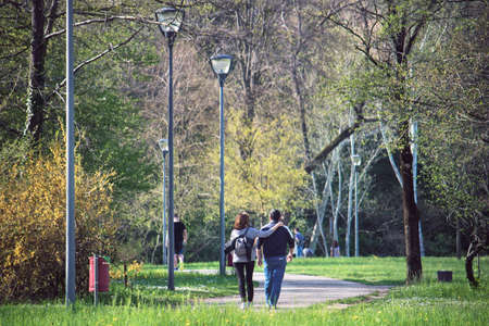 dates in park in springtime. Back view of couple - woman hugs her boyfriendの写真素材