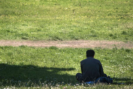 lonely man sitting on grass, back view of a person at the parkの写真素材