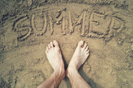 summer word written on the sand. Top view of human feet on summer beachの写真素材