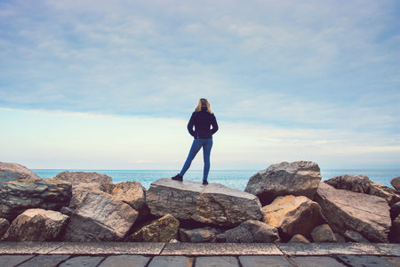 lonely woman on the rock at the seaside, blonde lady looking at the sea
