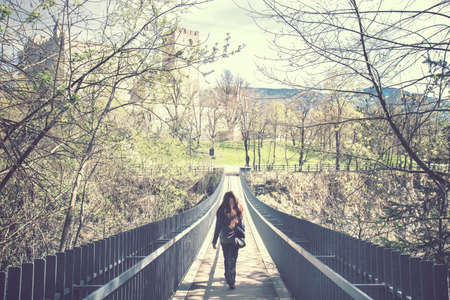 lonely girl crosses a bridge, on the top of picture there is Brunico's castle in Trentino Alto Adige, Italyの写真素材
