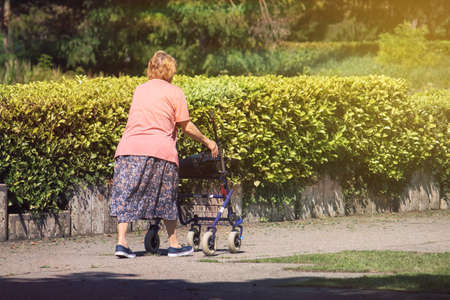 old lady with a walking disability, senior adult woman pushing a frame with wheels outdoorsの写真素材